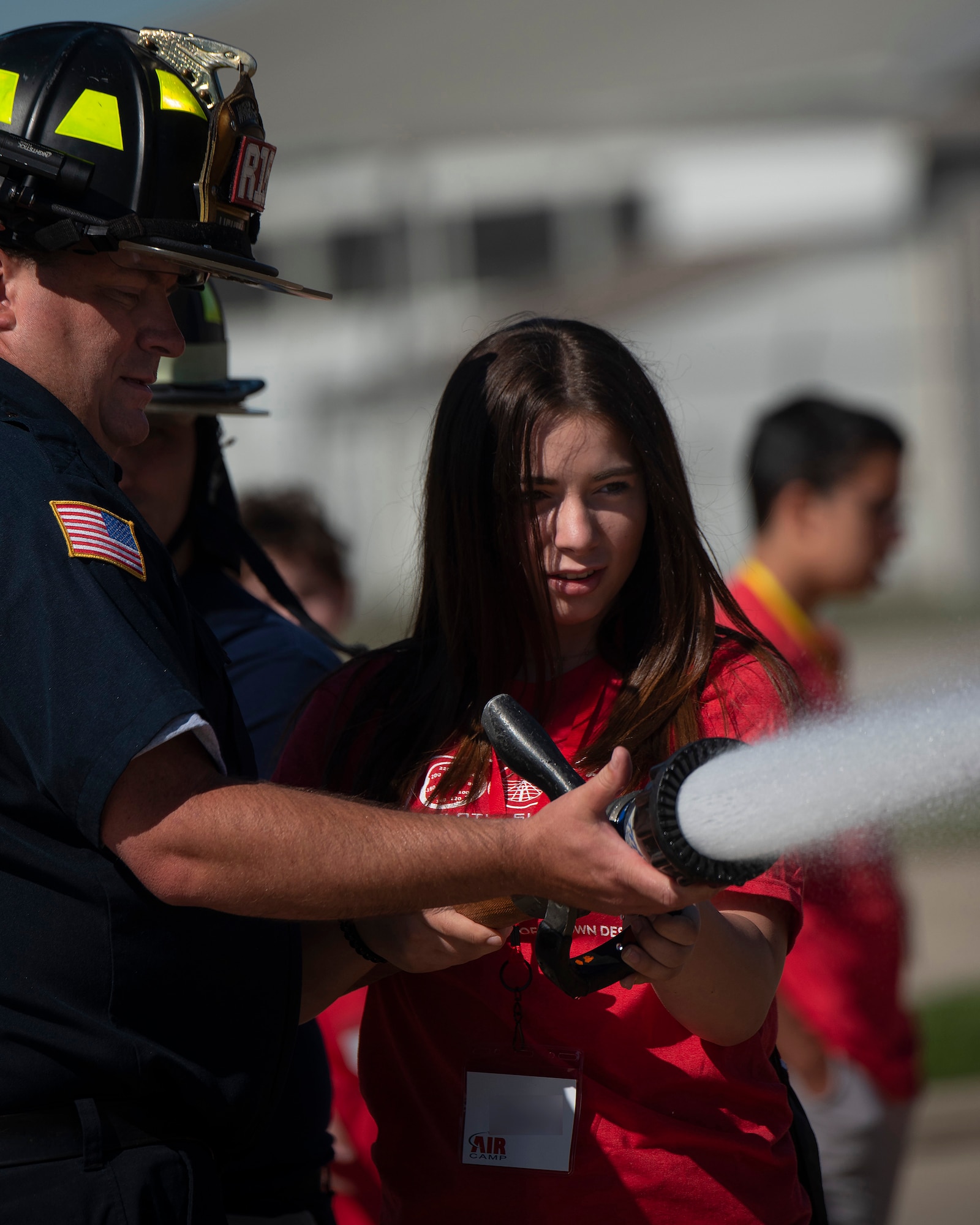 A camper handles a fire hose with the help of firefighter Thomas Trost, 788th Civil Engineer Squadron, at the main fire station on Wright-Patterson Air Force Base, Ohio, June 15, 2021. Air Camp participants came to Wright-Patt to tour aircraft, learn about firefighting and visit the U.S. Air Force School of Aerospace Medicine. (U.S. Air Force photo by R.J. Oriez) (Name tag blurred for security and privacy)