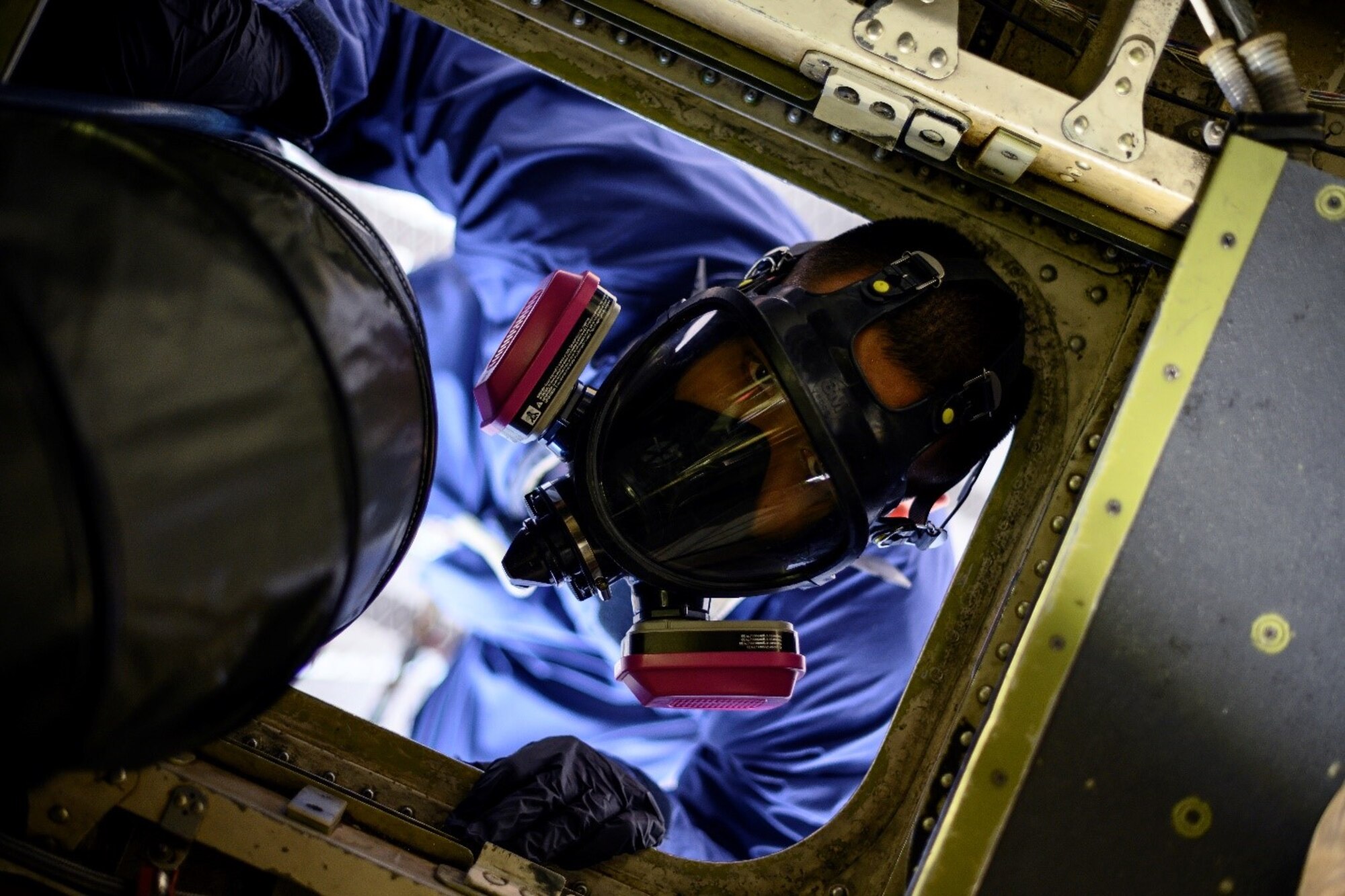 An Airman in a respirator looks up into a compartment of an aircraft.