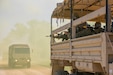 Soldiers man weapons while riding in a military vehicle on a dusty road.