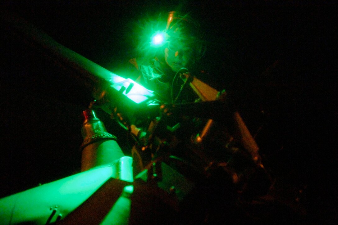 A sailor illuminated by green light works on an aircraft rotor at night.