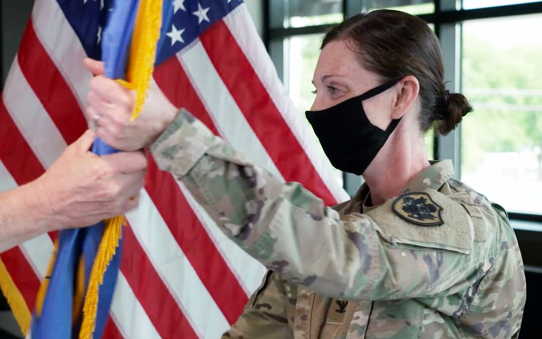 Masked female Army colonel takes flag as symbolic gesture of assuming command.