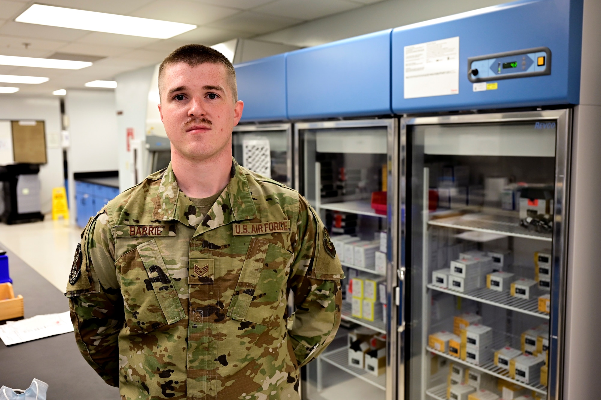 An Airman poses for a photo in front of a medical freezer.