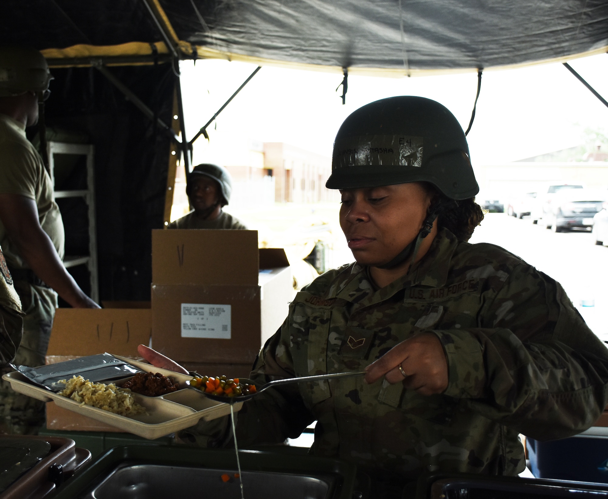 An Airman serves food on a paper tray in a field kitchen.