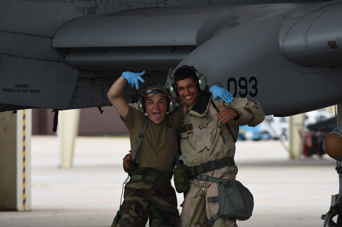 Two Airmen smile and pose for the camera in front of an A-10 Thunderbolt II attack aircraft.