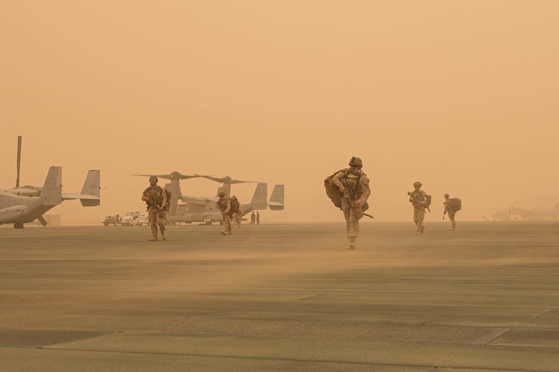 Marines walks on a dusty tarmac near aircraft.