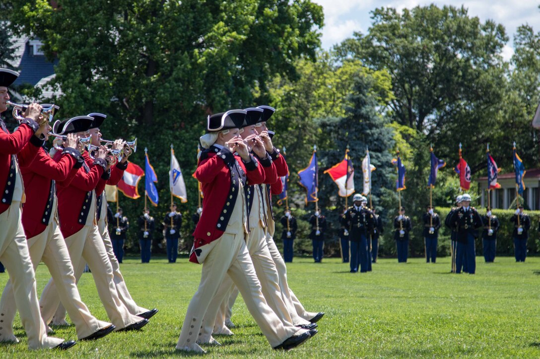 Soldiers dressed in period uniforms play instruments and march in formation.