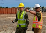 man points in distance while talking to another man, both in safety vest