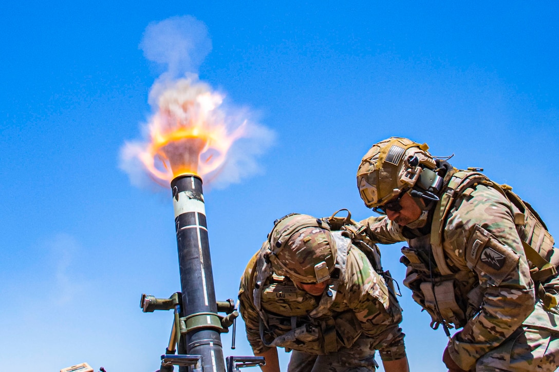 Two soldiers stand next to a mortar that has been fired.