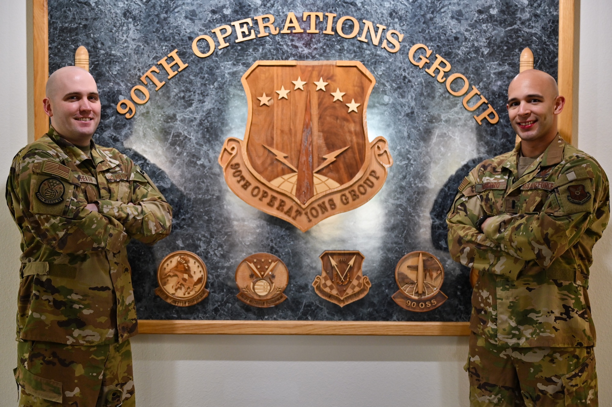 Capt. Christian Heath and 1st Lt. Juan Navarro, 321st Missile Squadron combat crew, pose in front of the 90th Operations Group emblem on F.E. Warren Air Force Base, Wyoming, June 17, 2021. The Air Force Association awarded Heath and Navarro the 2020 Gen. Thomas S. Power Outstanding Missile Crew Award. (U.S. Air Force photo by Joseph Coslett)