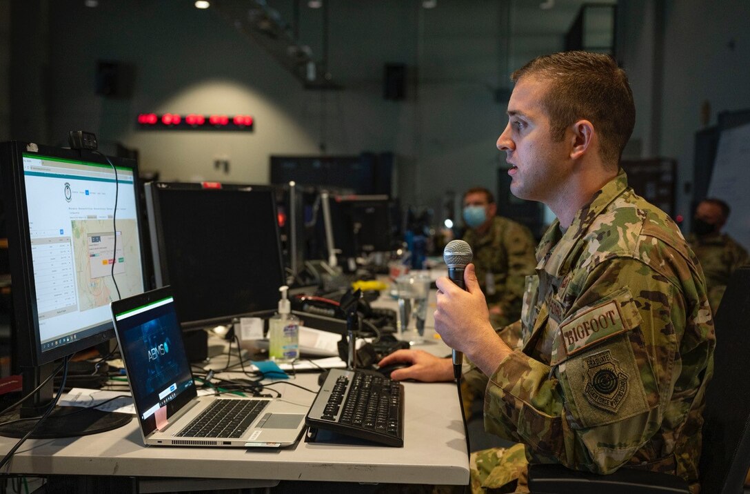An Airman holds a microphone while looking at a computer.