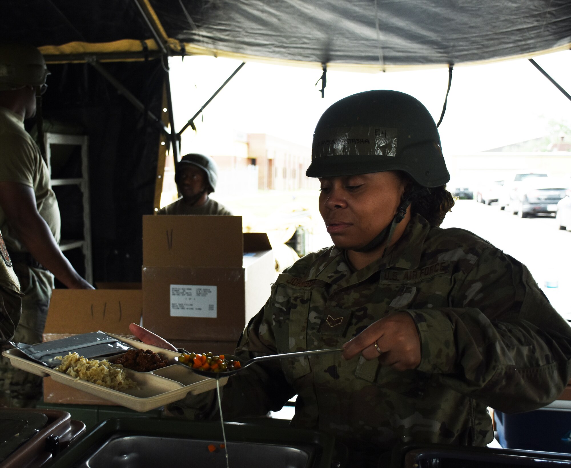 An Airman serves food on a paper tray in a field kitchen.
