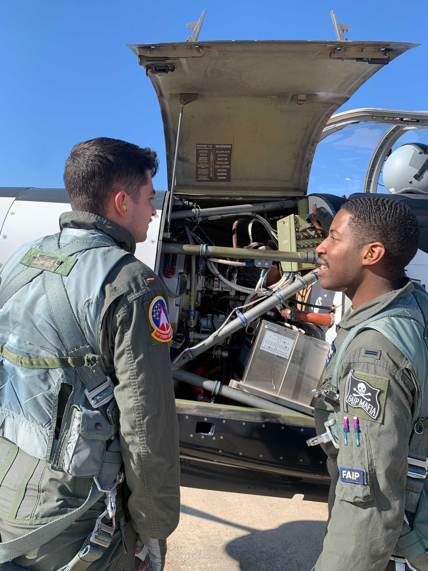 1Lt Courtland White stands outside air craft with 2Lt Skylar Reese, pointing at air frame