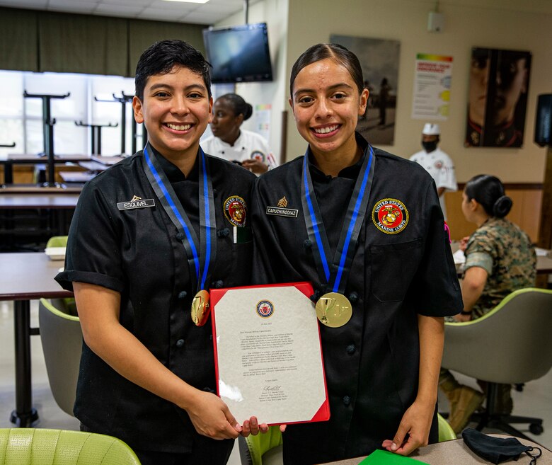 U.S. Marine Corps Lance Cpl. Marina Esquibel and Sgt. Morelia Capuchino-Diaz, food service specialists with 3d Marine Division, pose with their awards after the food service specialist of the quarter competition on Camp Kinser, Okinawa, Japan, June 16, 2021. The two-day competition began with a written and oral examination where Marines are judged on their military appearance, knowledge, and bearing. The second portion of the event focused on the Marines’ culinary, sanitation and nutritionary skills while under the watchful eye of quality assurance evaluators. Esquibel is a native of San Antonio, Texas, and Capuchino-Diaz is a native of Goshen, Indiana. (U.S. Marine Corps photo by Lance Cpl. Alex Fairchild)