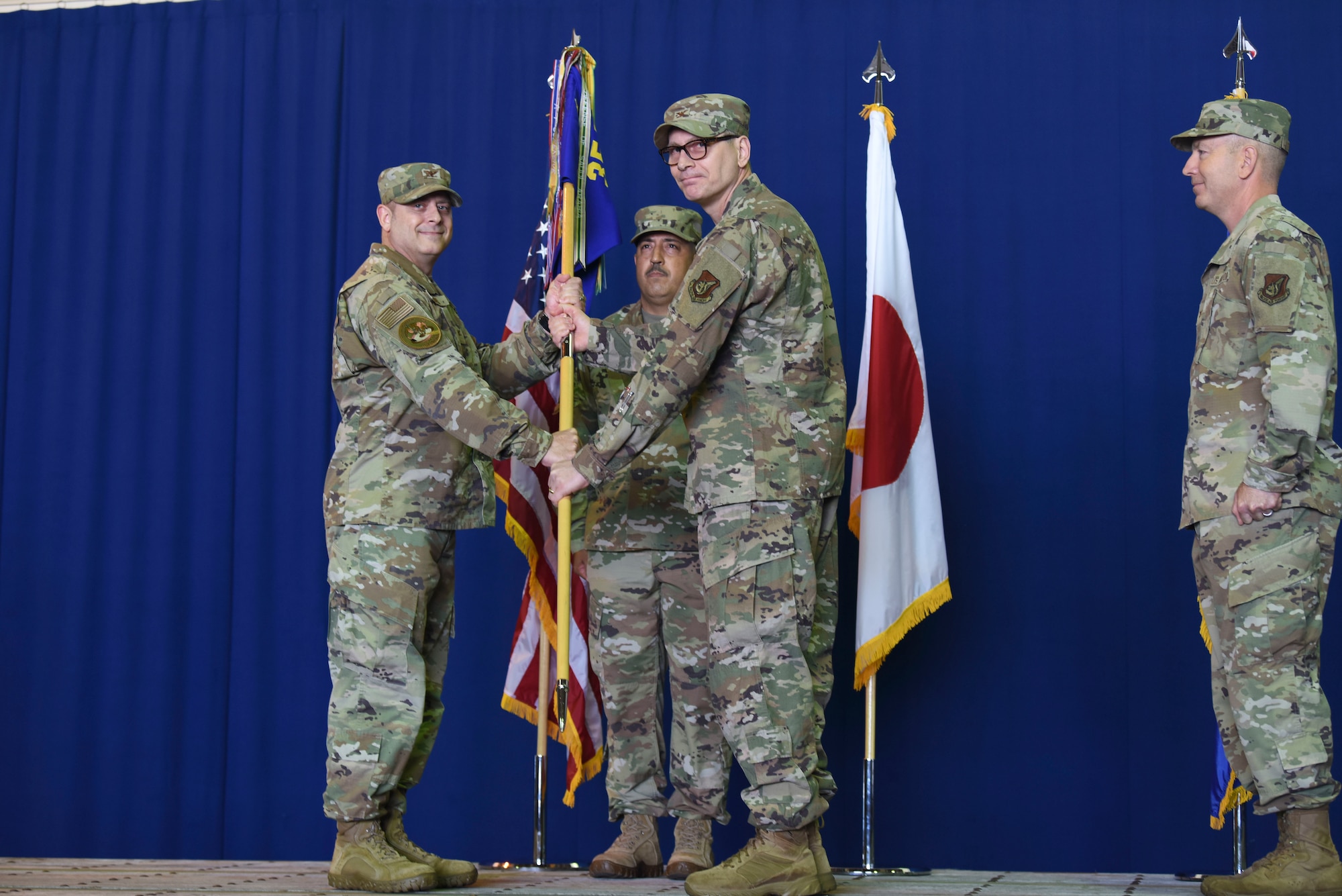 Two uniformed military members hold a guidon while looking at a picture.
