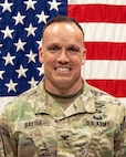 photo of a man standing in front of a flag.