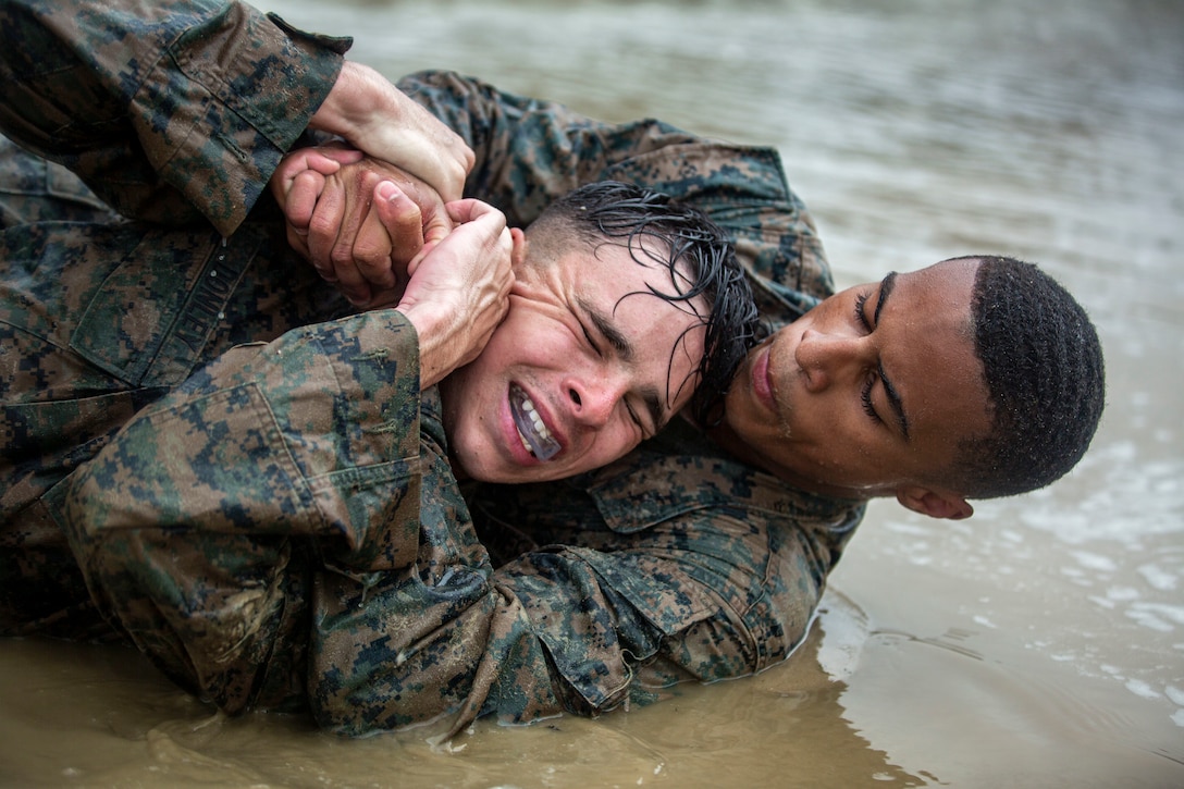 Two Marines fight in muddy water.