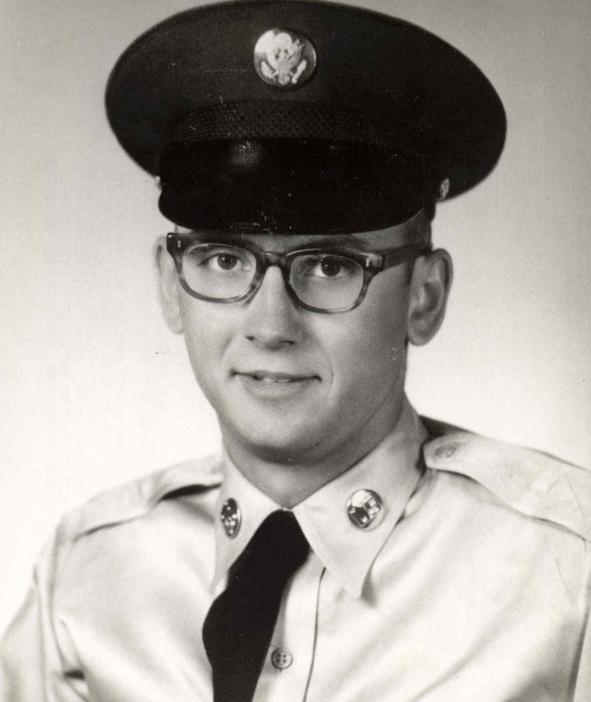 A young man with glasses in a military uniform looks at the camera.