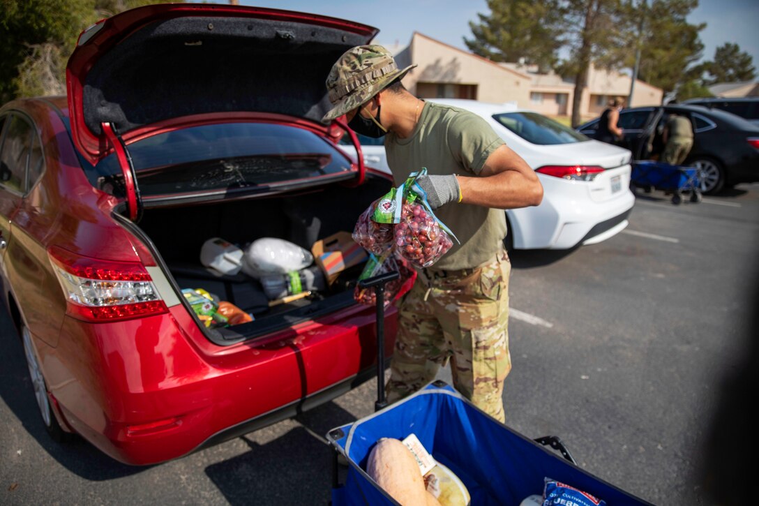 A soldier wearing a face mask and gloves load groceries into the trunk of a car for a local resident.