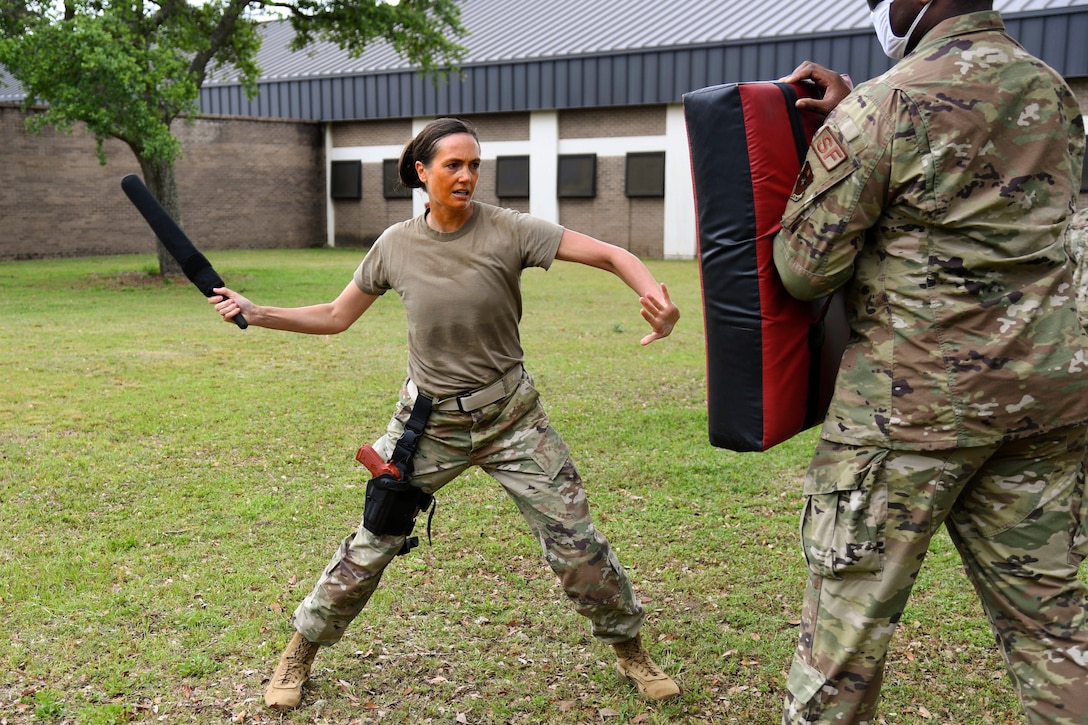 An airman aims a baton at a pad being held by another airman.
