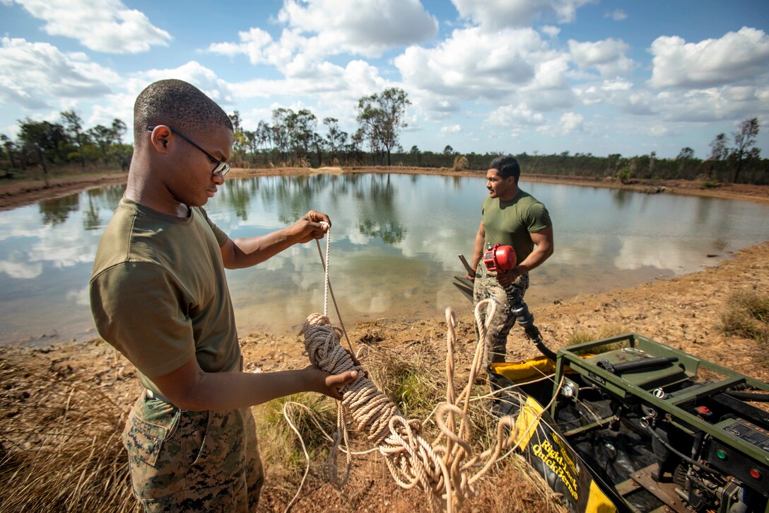 Two Marines set up a system next to water in the woods.