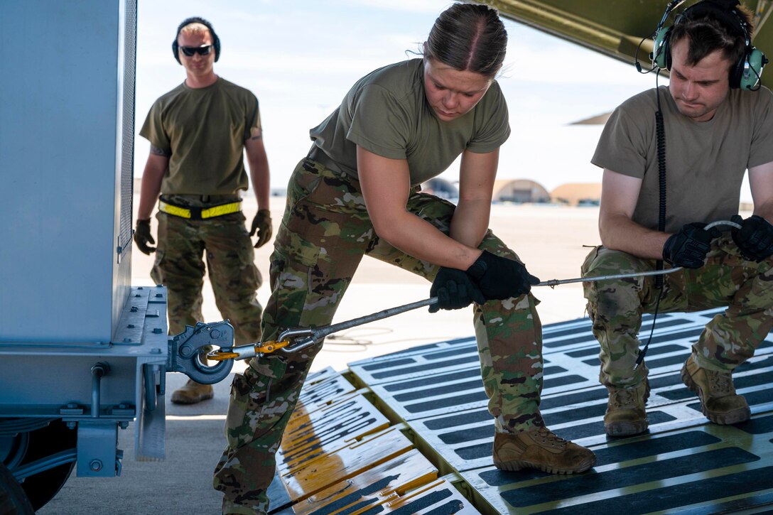 An airman pulls a rope attached to equipment as two others watch.