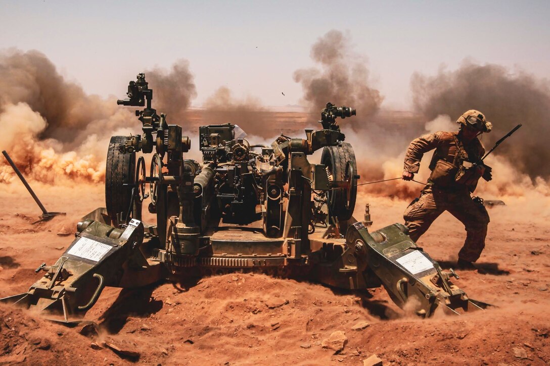 A Marine fires a howitzer as dust rises from the ground.