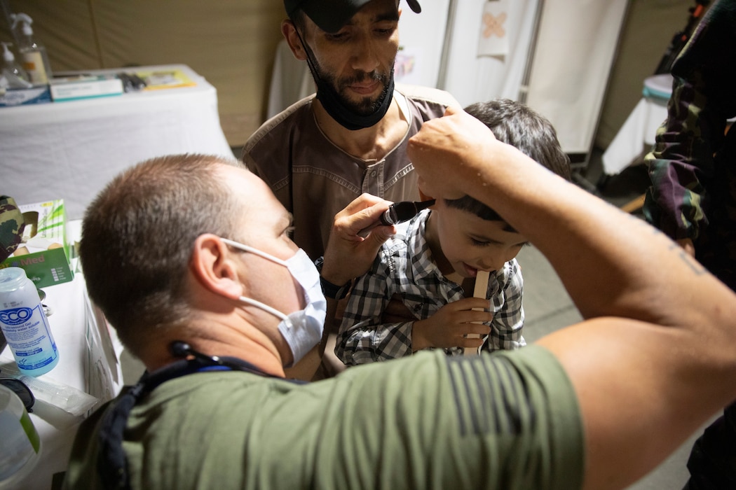 A U.S. military physician assistant inserts a medical instrument into the ear of a Moroccan boy while the boys father looks on.