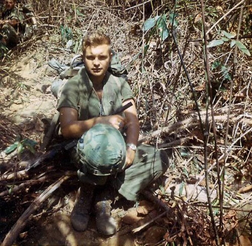 A soldier kneels in jungle terrain.