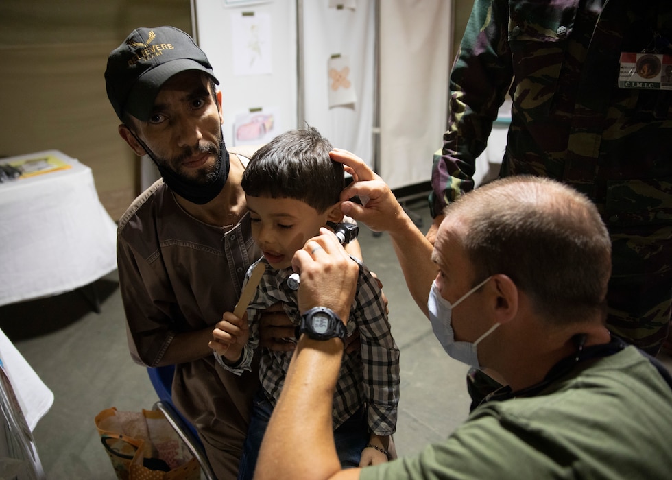 A U.S. military physician assistant inserts a medical instrument into the ear of a Moroccan boy while the boys father looks on.