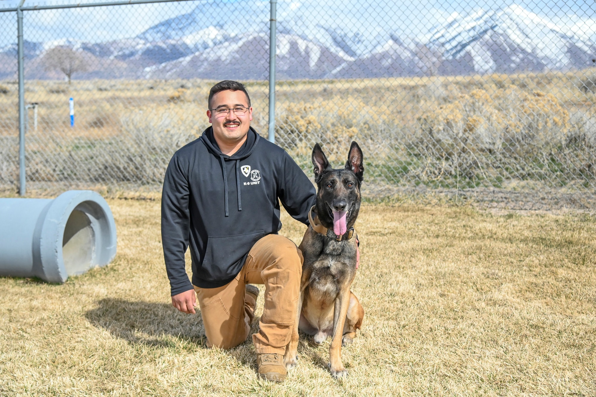 Posing for the camera, Staff Sgt. Reyes crouches on one knee next to retired military working dog Cvoky who is sitting.