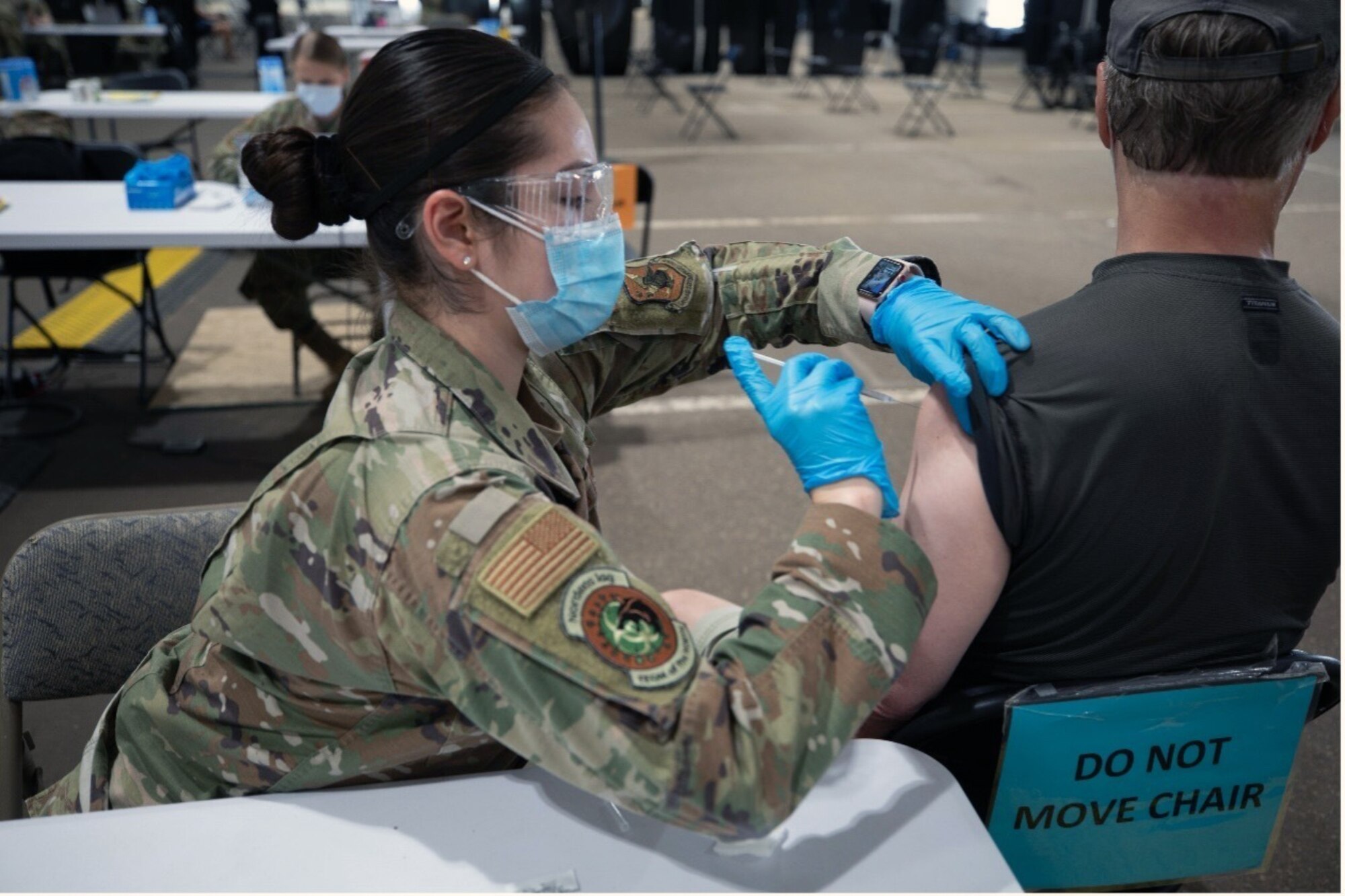 Female military member administering vaccine to patient.