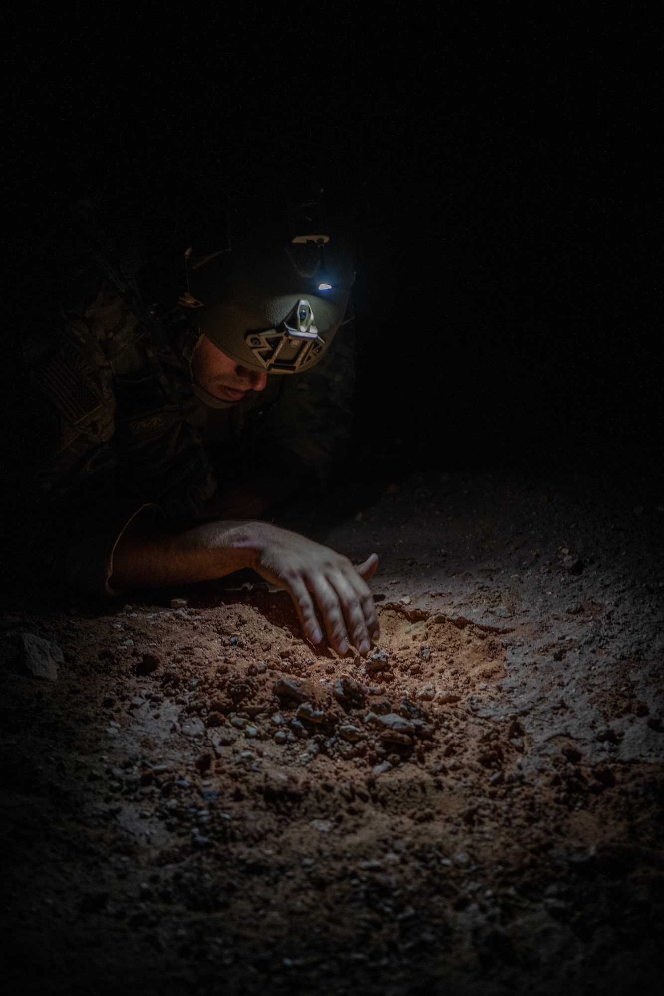 U.S. Air Force Staff Sgt. Gideon Hanes, 378th Expeditionary Civil Engineer Squadron Explosive Ordnance Disposal team lead, slowly digs through dirt in search of a simulated improvised explosive device during a quick response training event in blackout conditions at Prince Sultan Air Base, Kingdom of Saudi Arabia, June 12, 2021. PSAB EOD, Security Forces and Medical personnel participated in integrated training to bolster defensive capabilities and maintain readiness at all times. (U.S. Air Force photo by Capt. Rachel Buitrago)