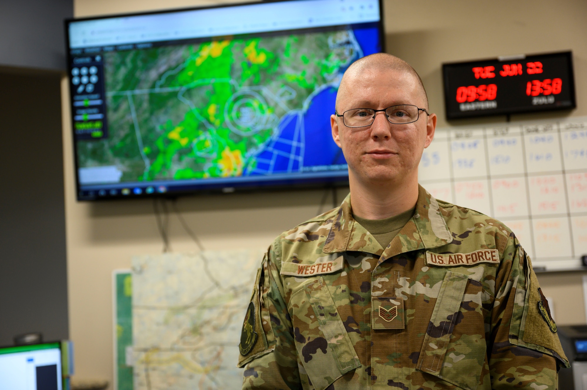 A photo of Staff Sergeant Travis Wester posing in front of weather screen.