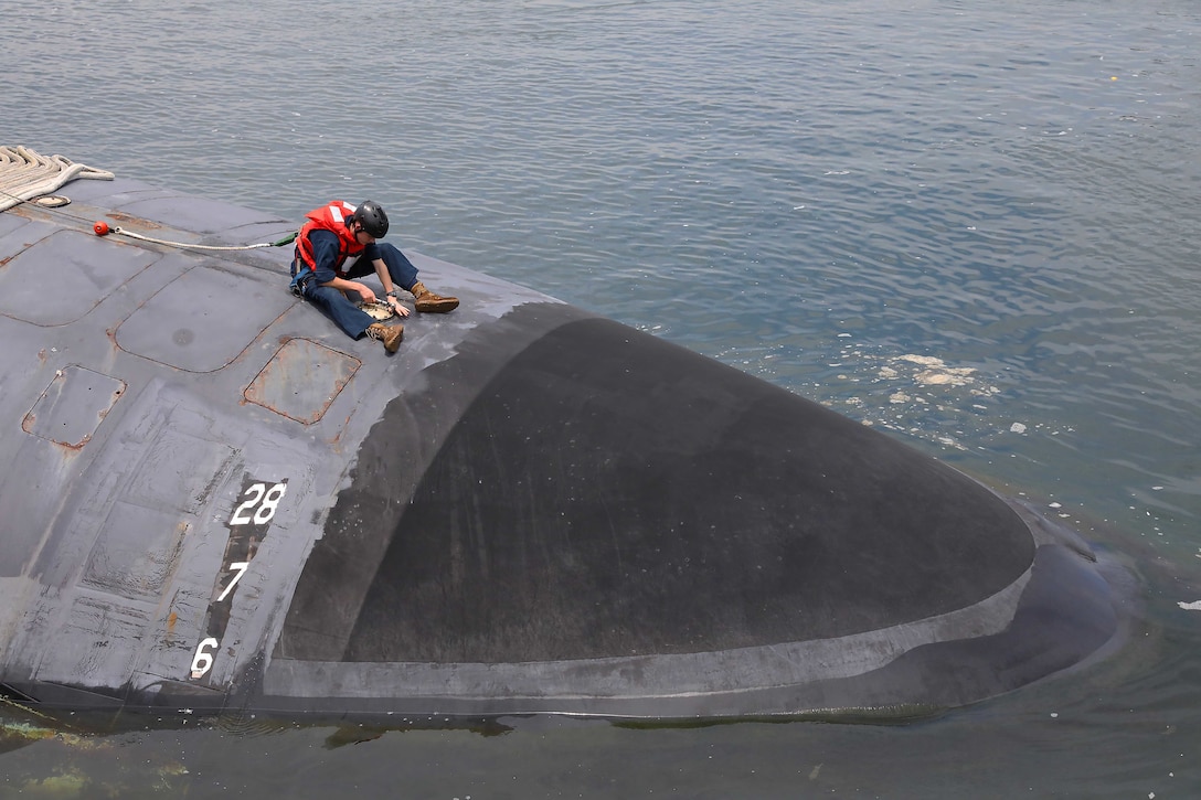 A sailor works on the top of a submarine.