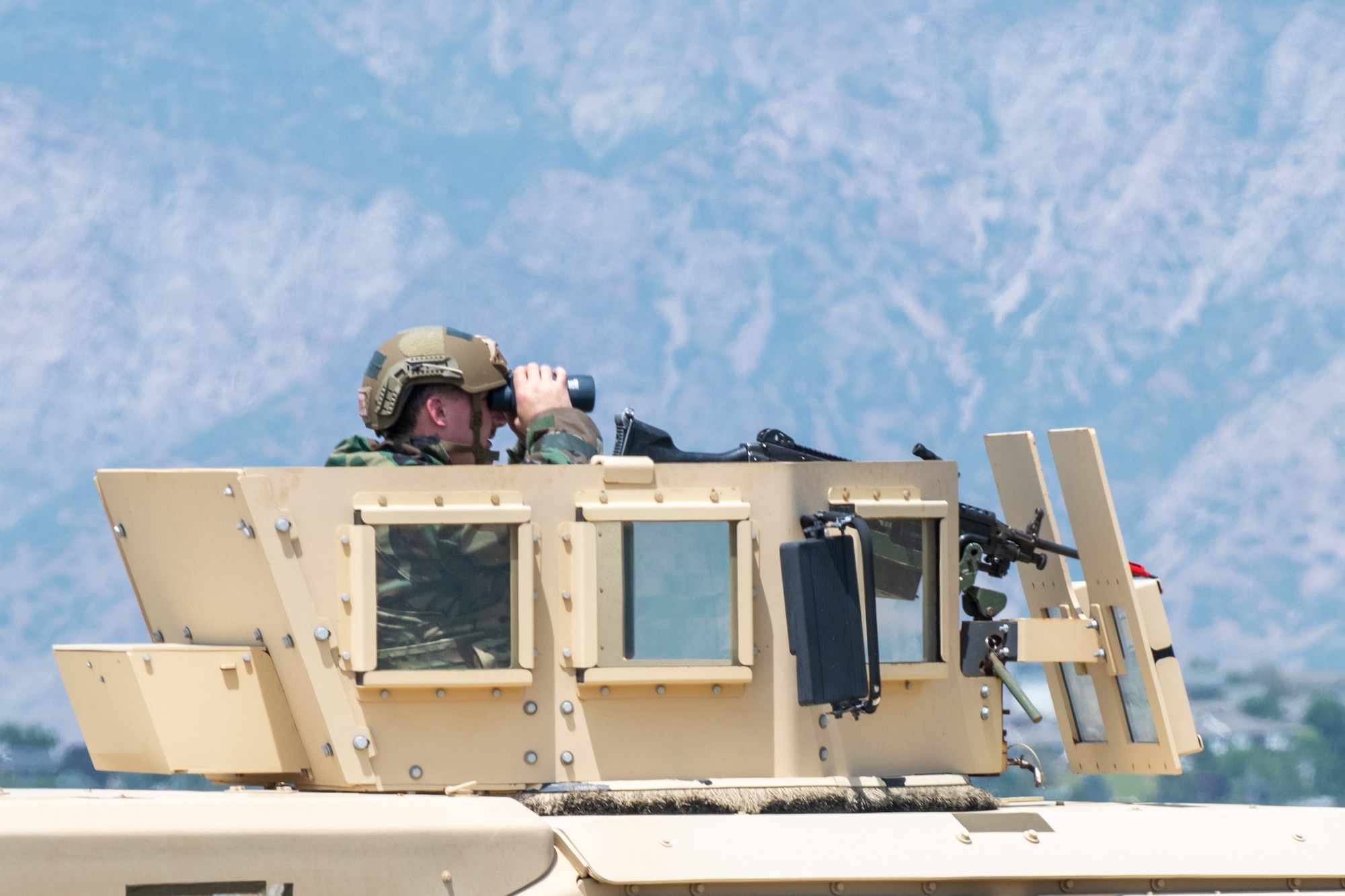 An Airmen inside the turret on a Humvee looking through binoculars.