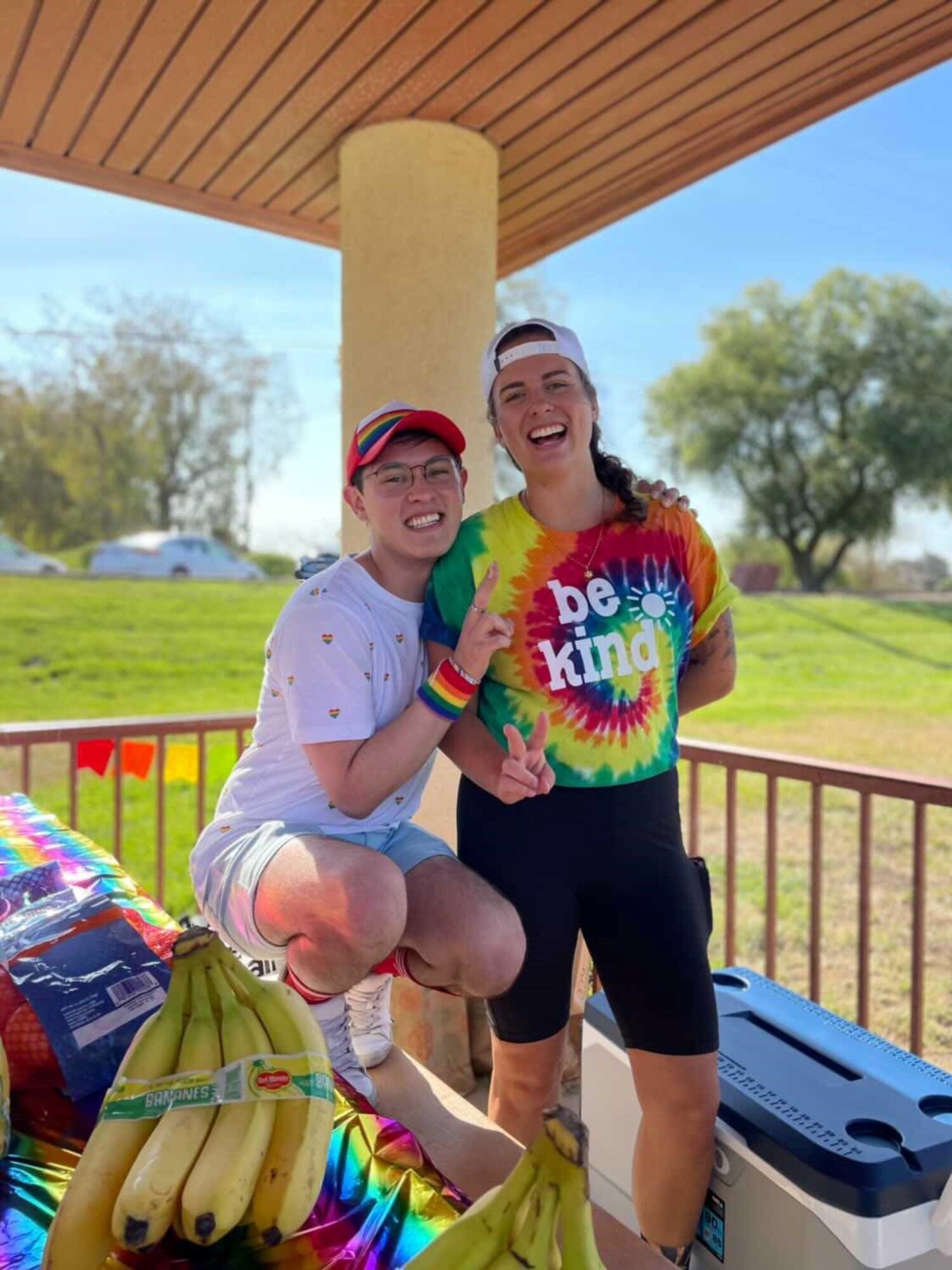 Two people in pro-LGBTQ+ attire pose for a picture at a picnic table outside