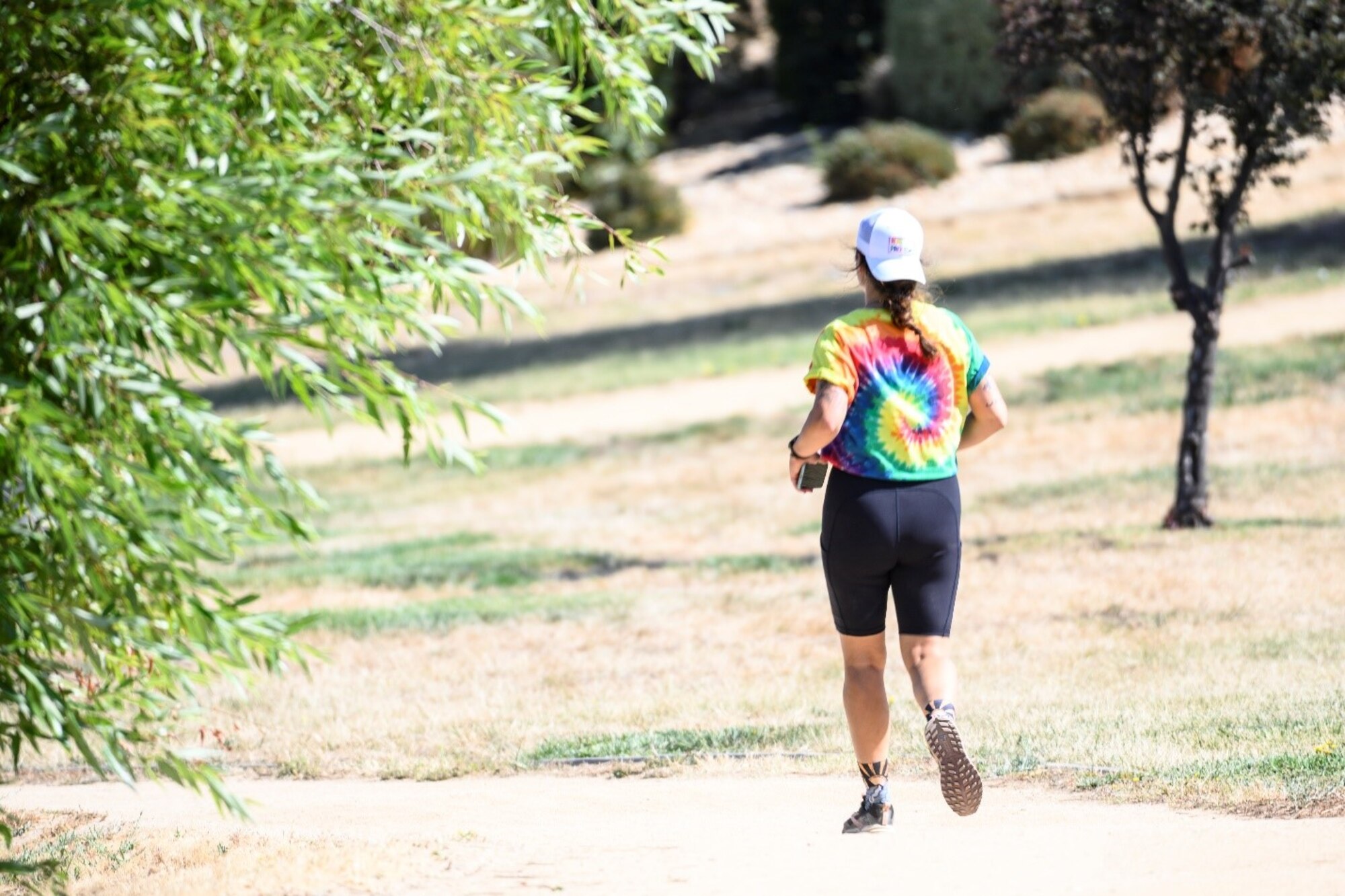 A person in a rainbow tie-dye shirt runs on a dirt path