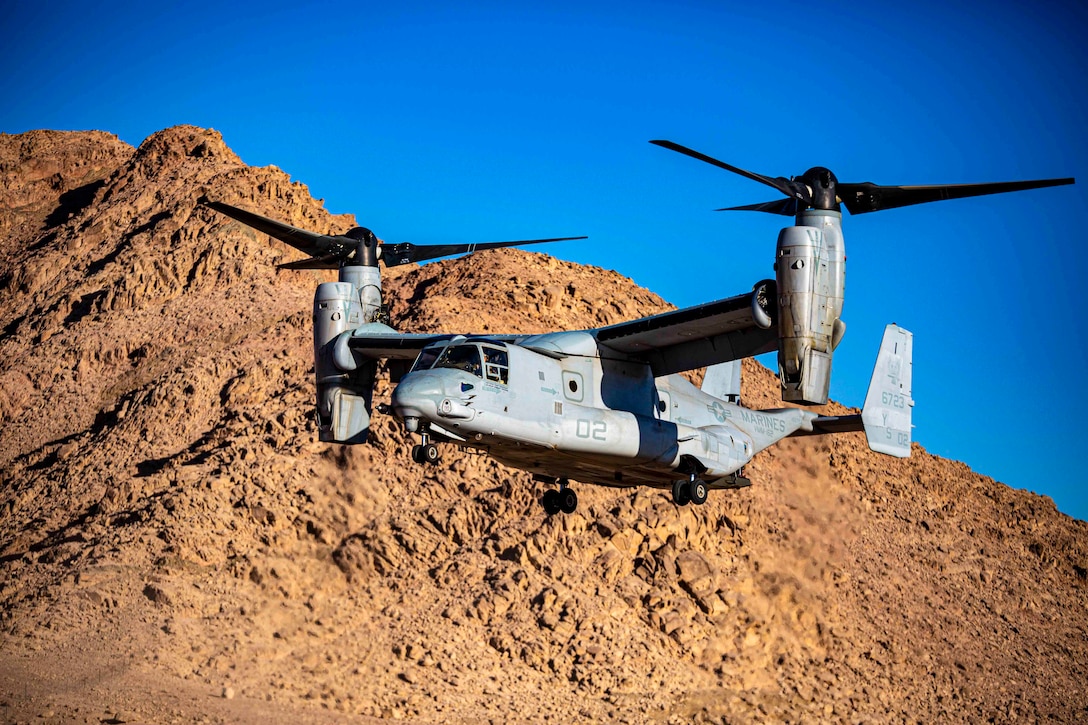 An MV-22B Osprey flies in front of a mountain.