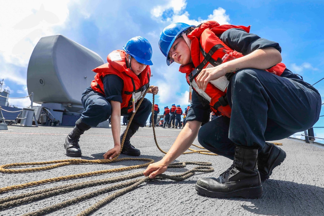 Two sailors arrange rope on the deck of a ship.