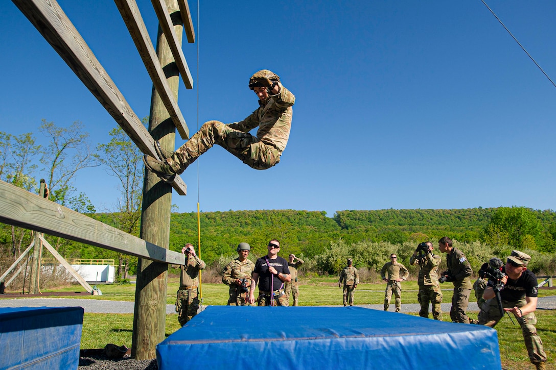 A soldier falls backwards onto a mat as others watch.