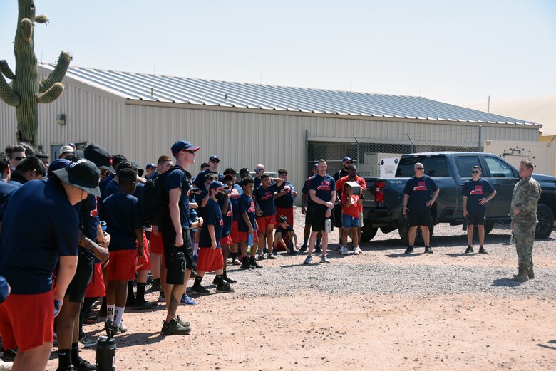 A photo of Children gathered around a military instructor as he explains his teams occupation.