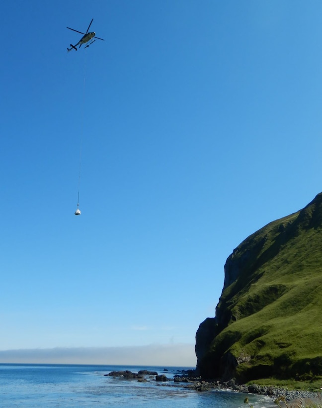 A helicopter slings contaminated soil from the upper camp to the lower camp at the Cape Prominence Formerly Used Defense Site.