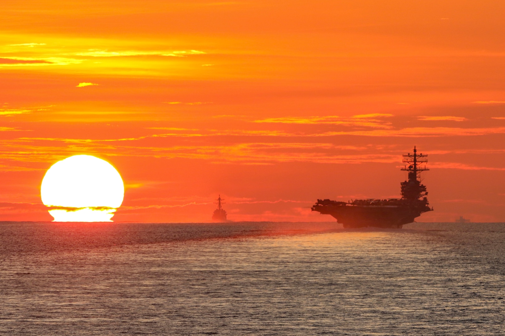 Three  ships transit a body of water under a sunlit sky.