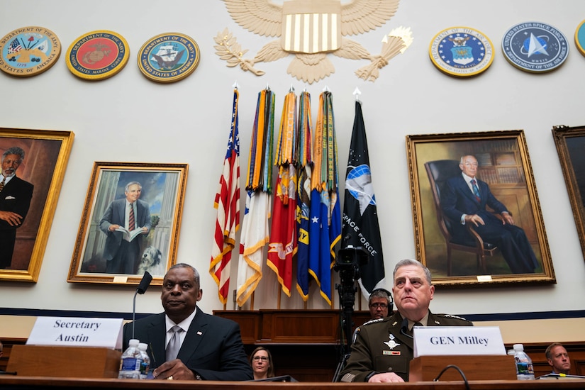 Secretary of Defense Lloyd J. Austin III and Army Gen. Mark A. Milley, chairman of the Joint Chiefs of Staff, testify in a large room with flags behind them.