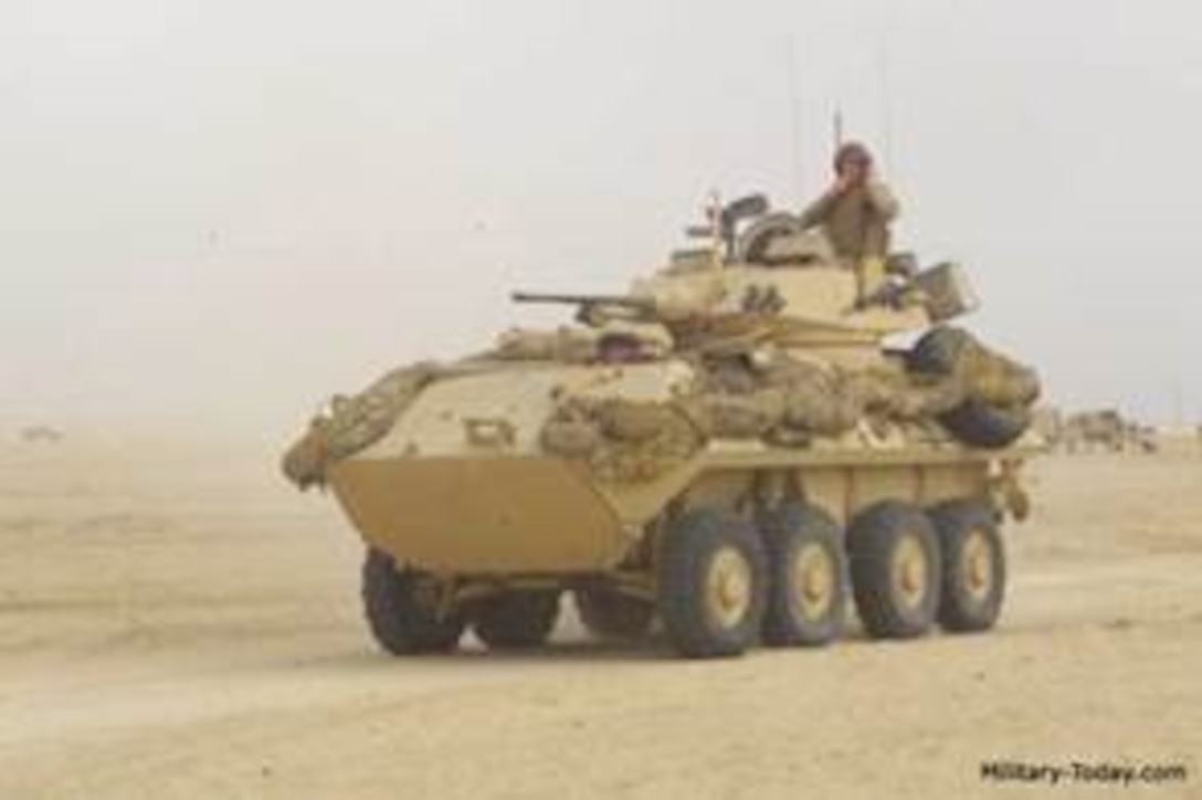 Eight-wheeled KMA Stryker vehicle rolling toward the camera in a desert setting with a service member sitting on top.