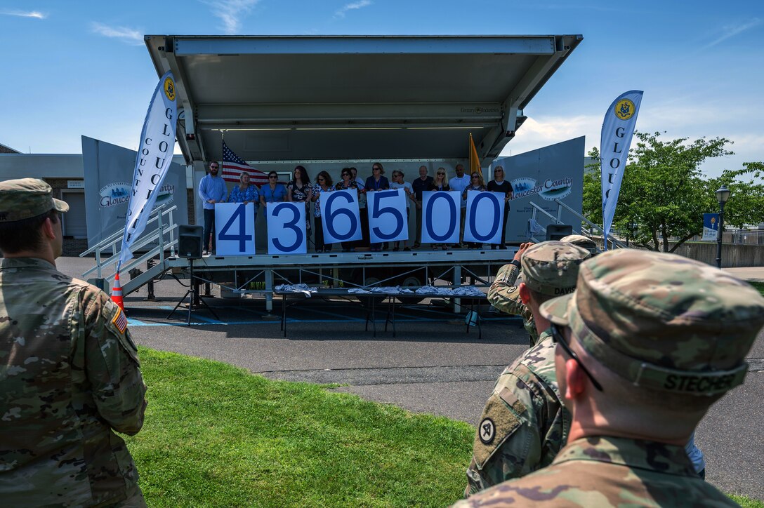 Health care workers hold up signs showing the number of vaccines given out.