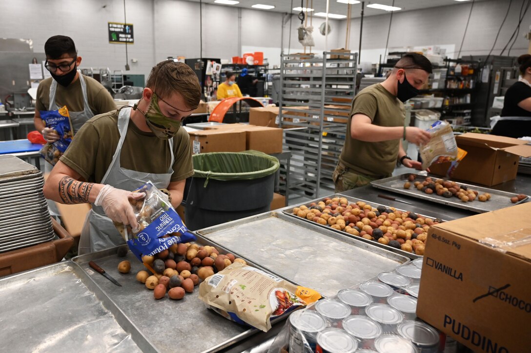 Guardsmen wearing face masks and gloves pour potatoes onto a tray.