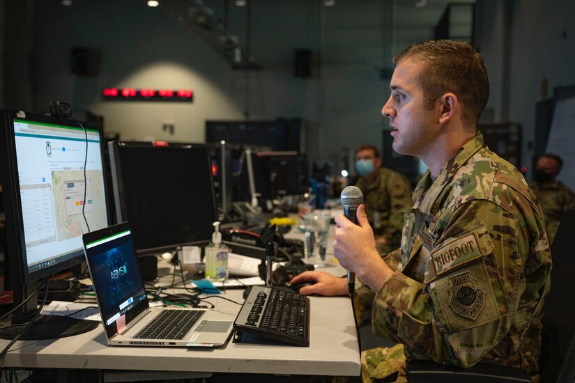 An airman speaks through a microphone as he looks at a computer screen.