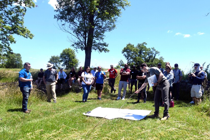 A group of people stand around a map lying on the ground.