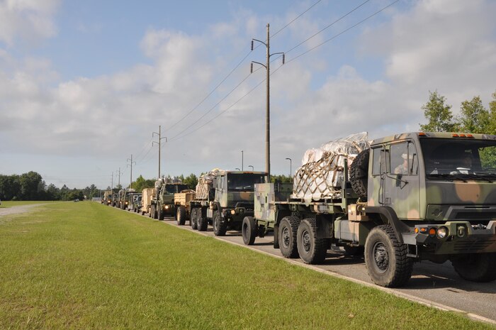 Photo shows line of military trucks driving down road.